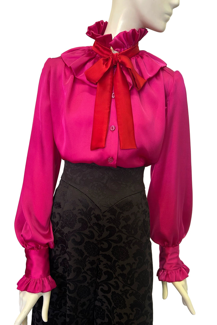 Mannequin wearing Estelle jazz satin blouse - a bright pink blouse with a large red bow and a black lace skirt.