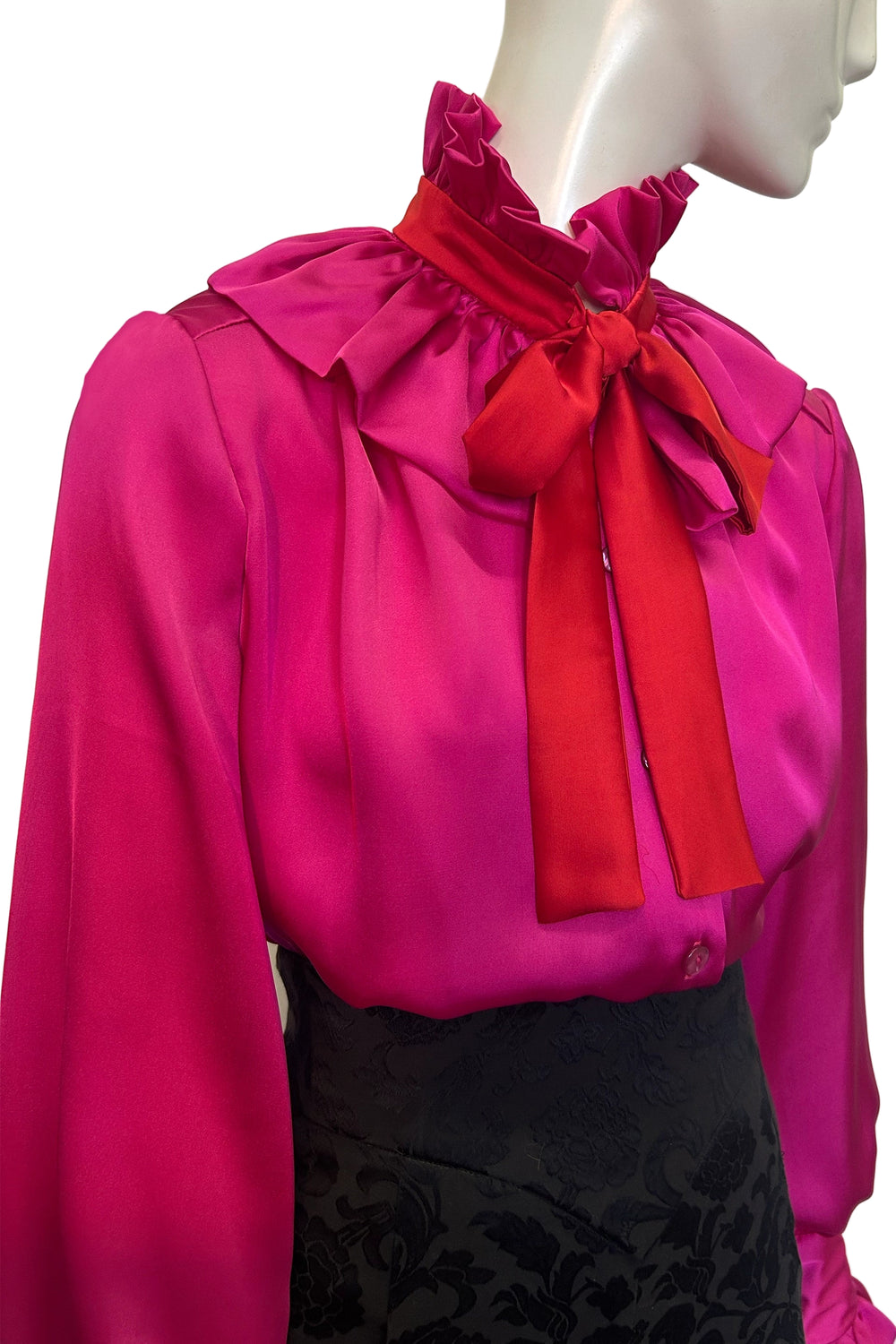 Mannequin wearing the Estelle Jazz satin blouse by Holly Campbell. A bright pink blouse with a large red bow against a white background