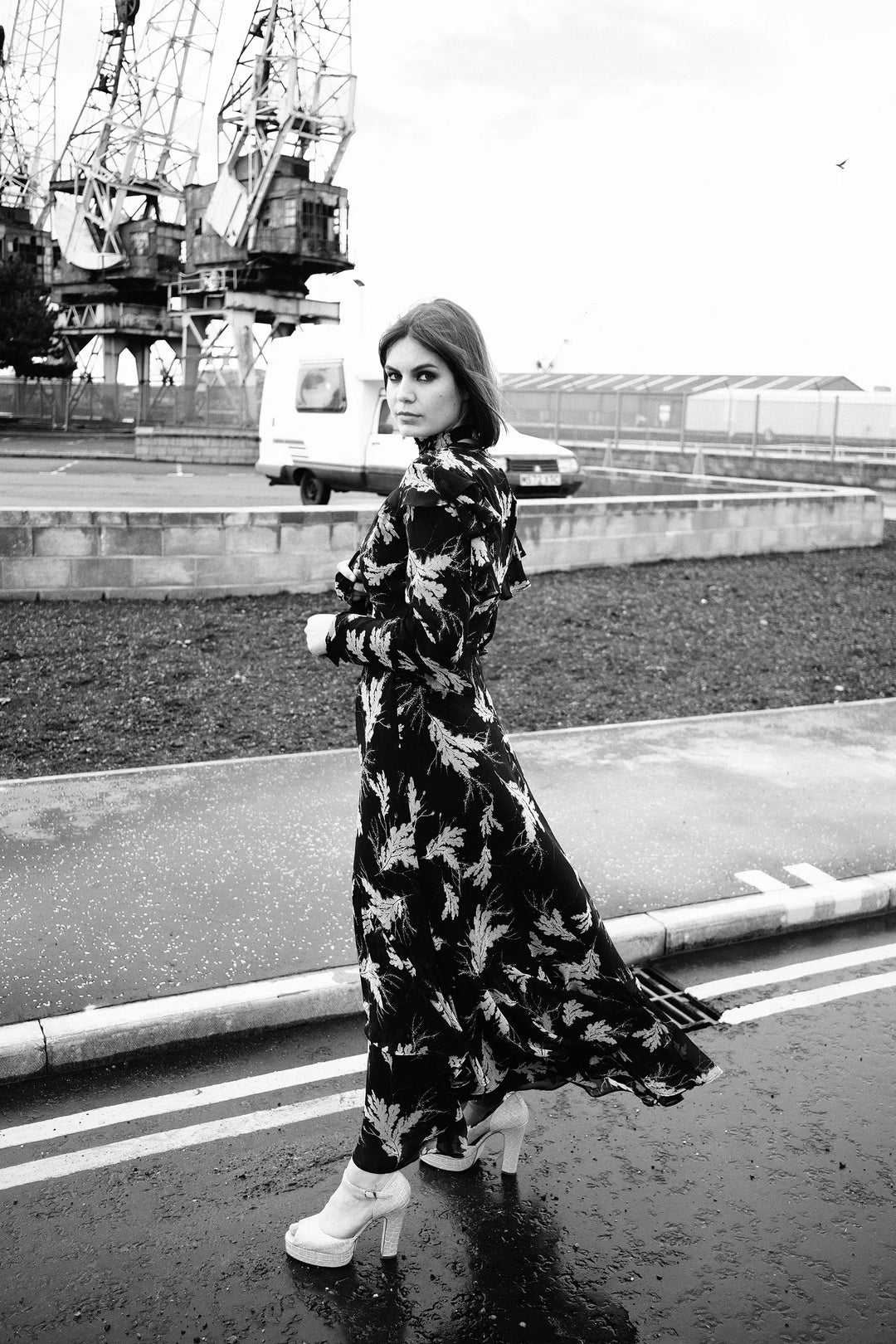 Model is standing at Leith Docks wearing the long Angie dress with a floral pattern, blown by the wind.