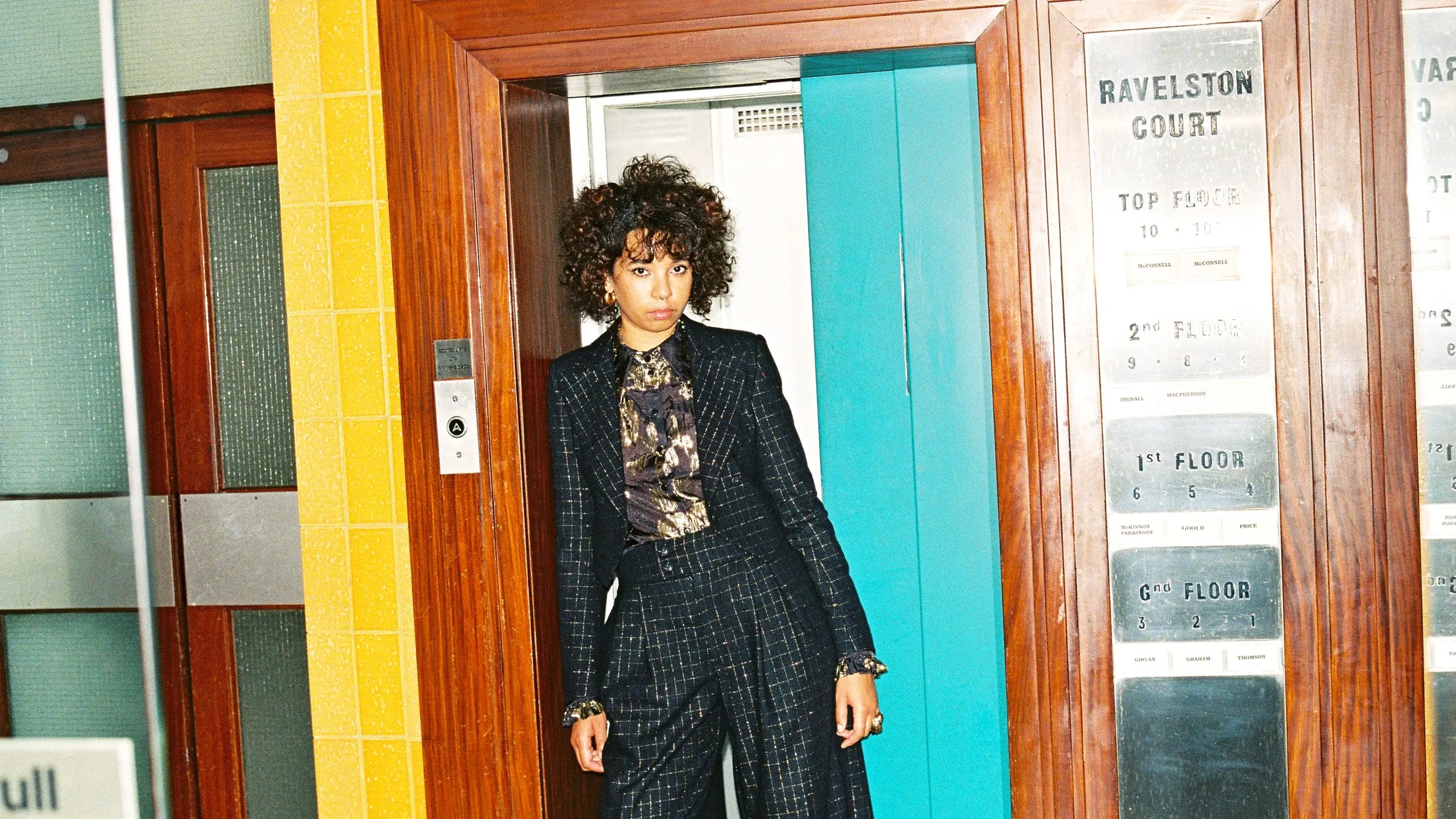 Person in a checkered suit standing in front of a door with a sign on it.